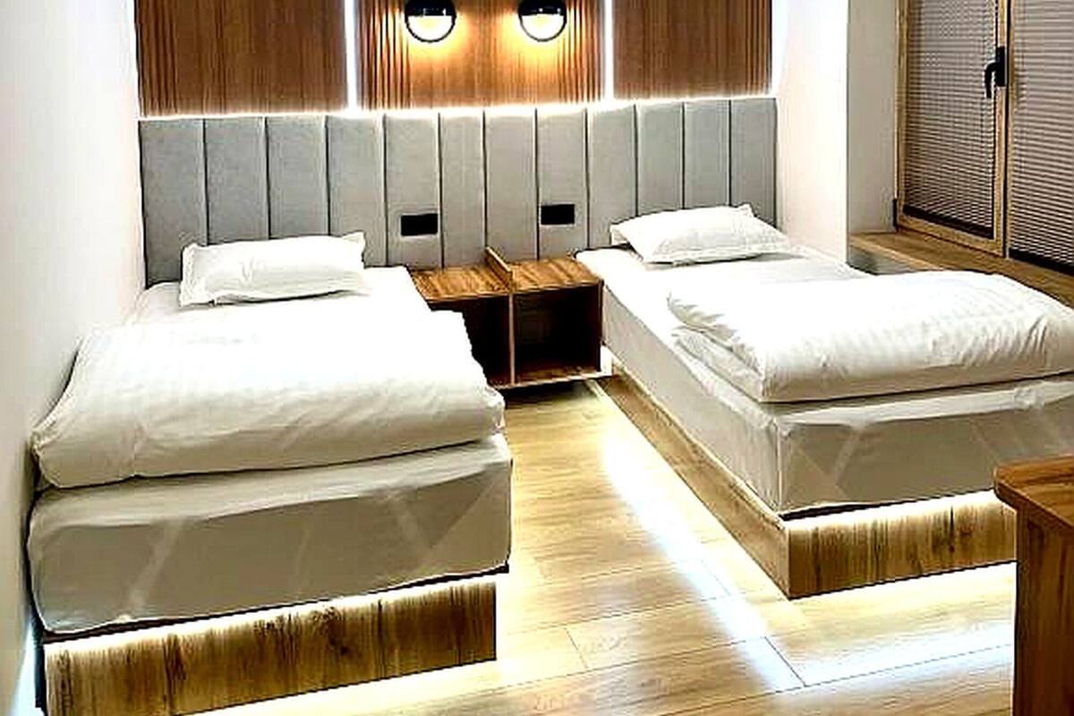 Un dormitorio moderno con dos camas, cabecero de madera, luces empotradas en el techo y una puerta corredera.