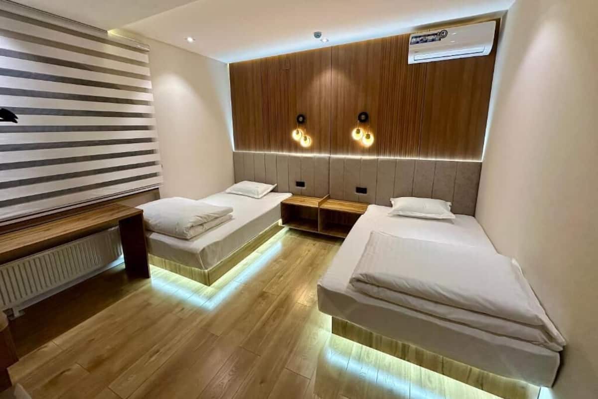 Habitación de hotel con dos camas individuales, cabecero de madera, radiador y aire acondicionado de pared.