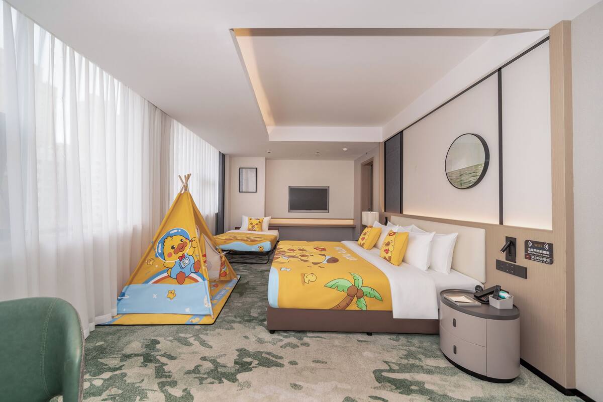 A hotel room with a bed, a small sofa, a nightstand, a mirror, and a window with curtains.
