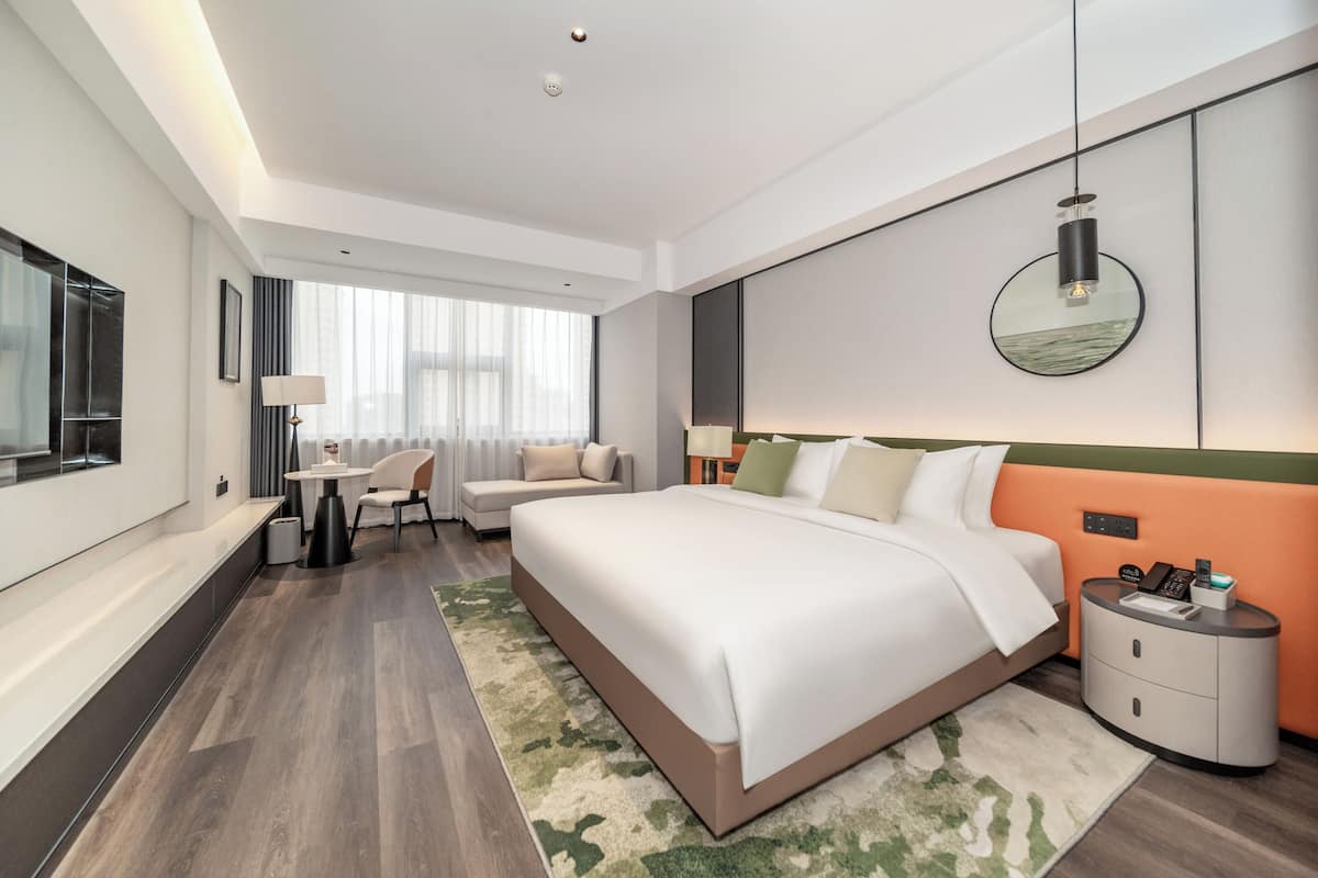 A modern hotel room with a large bed, bedside tables, a desk, and a chair.