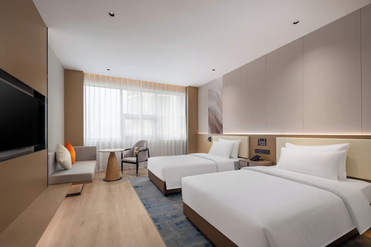 A hotel room with two beds, a sofa, a TV, a desk, and a window with curtains.
