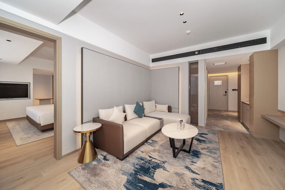 A modern hotel room with a sofa, two side tables, a TV, and a large mirror.
