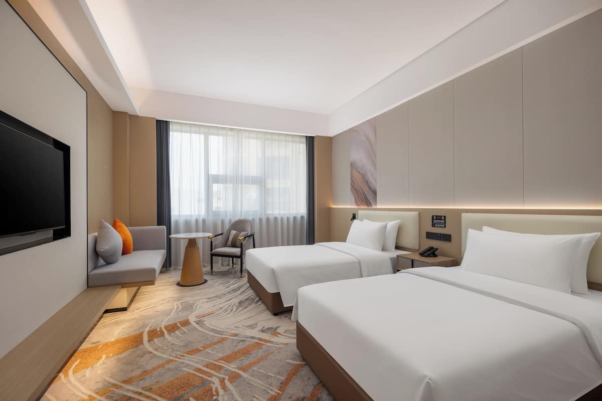 A hotel room with two beds, a sofa, a TV, a desk, and a window with curtains.
