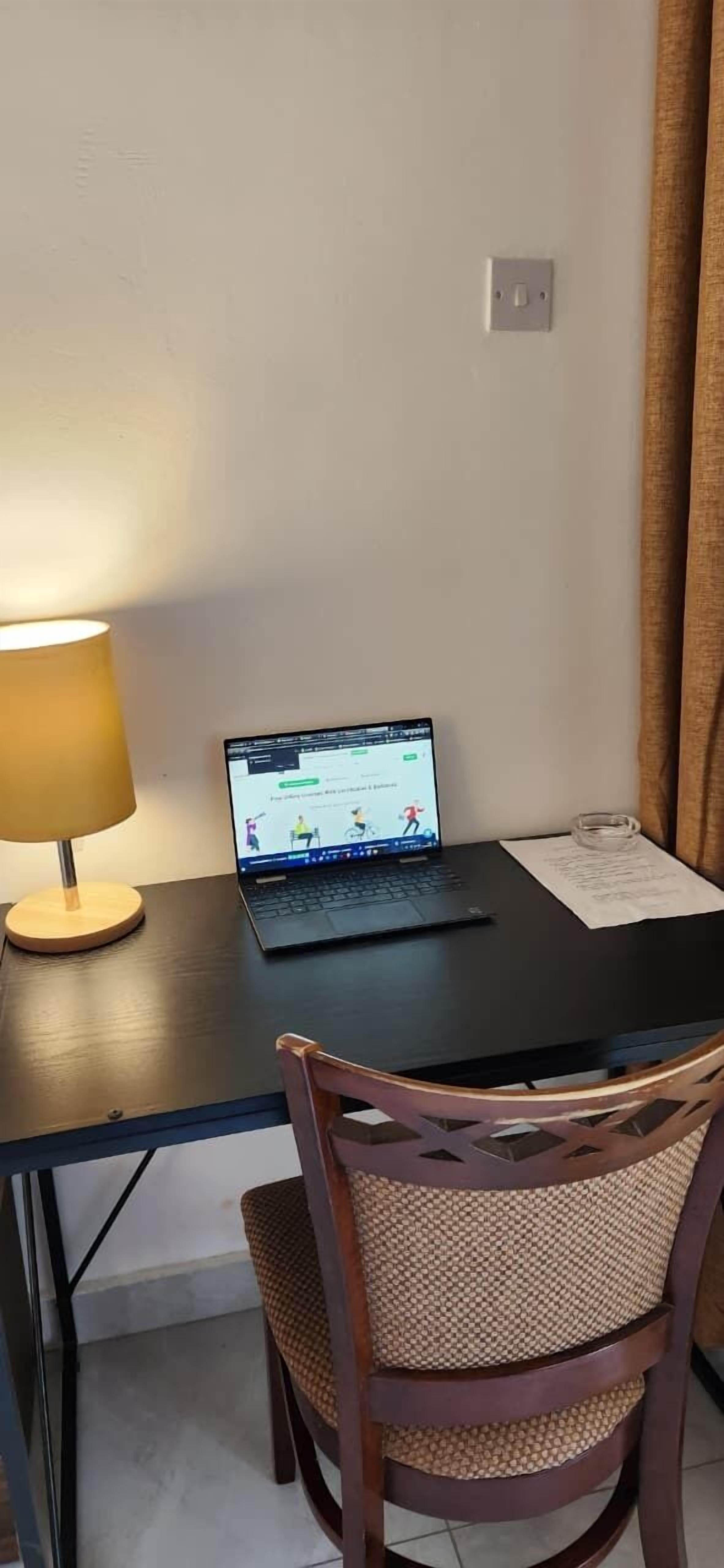 Una computadora portátil sobre una mesa con una lámpara, una silla y un enchufe de pared.