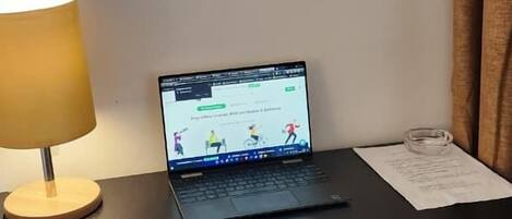 Una computadora portátil sobre una mesa con una lámpara, una silla y un enchufe de pared.