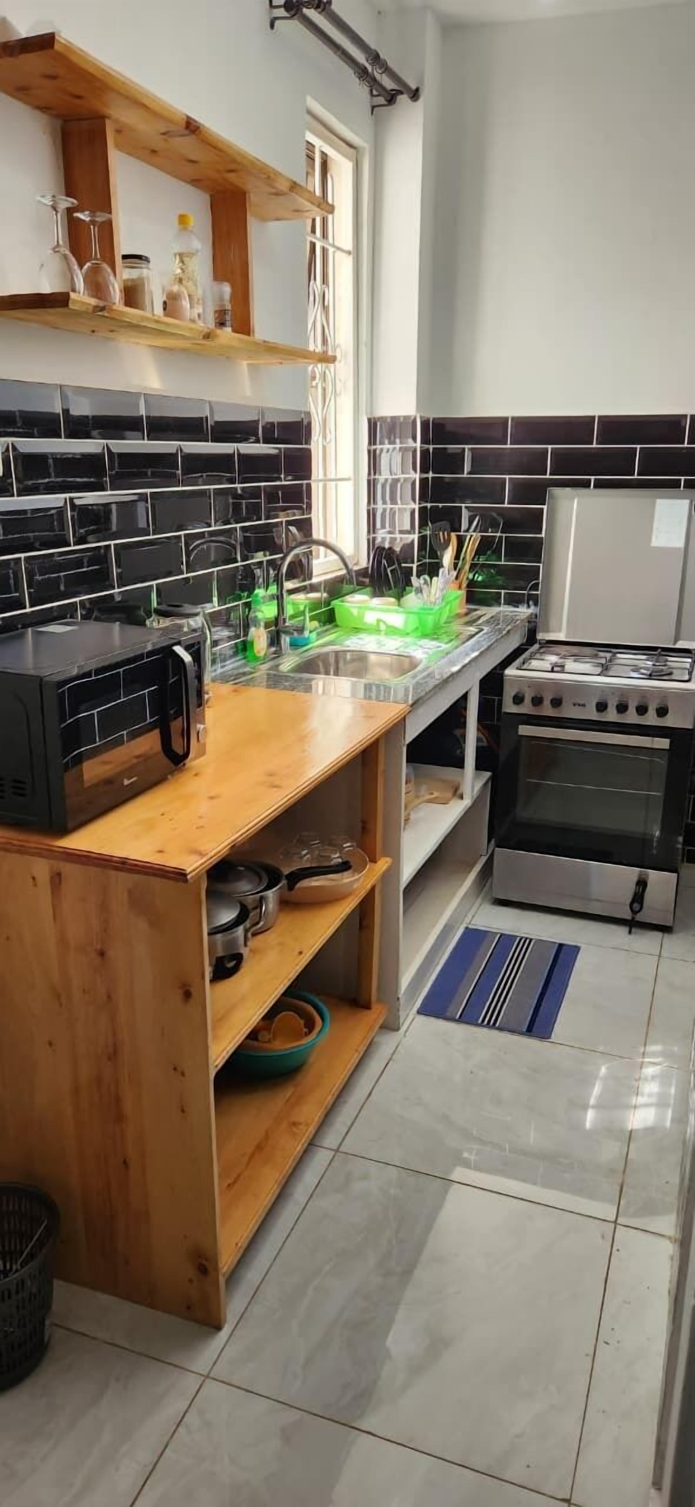 A kitchen with black and white tiled backsplash, wooden shelves, a stainless steel stove, and a sink.