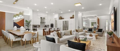 A modern living room with a dining area, kitchen, and a large window providing natural light.