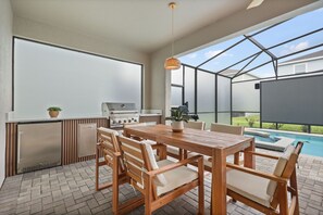 Eine Terrasse im Freien mit Holztisch und -stühlen, einem Grill und einem Pool.