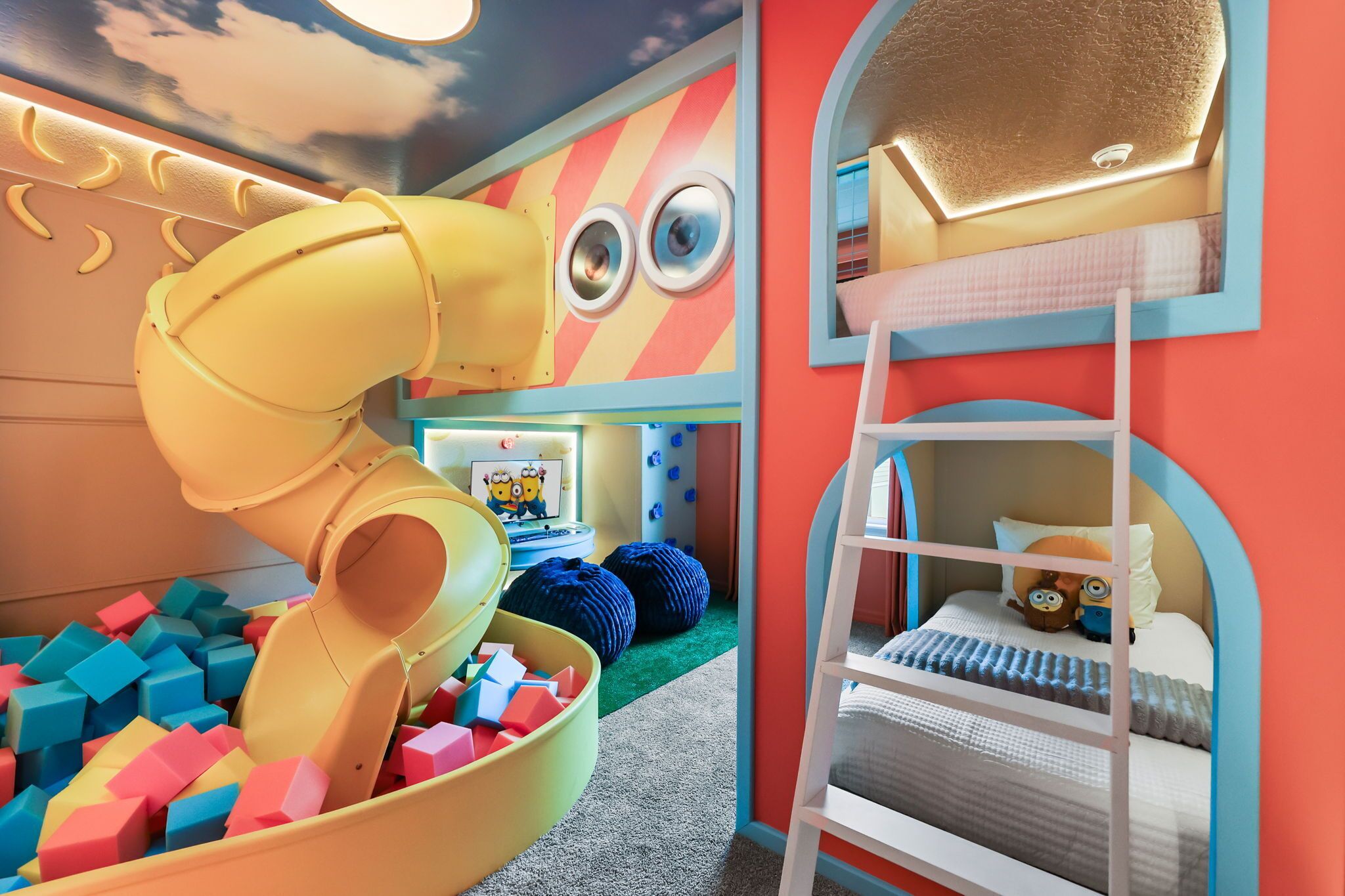 Et legeområde for børn med rutchebane, skumklodser og en køjeseng med en pude med Minion motiv.