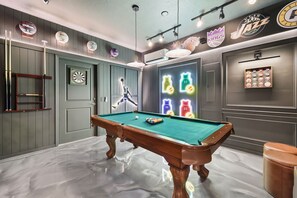 Ein Billardtisch mit einer Neon-Basketball-Reklame, eine Dartscheibe und ein Basketballkorb.