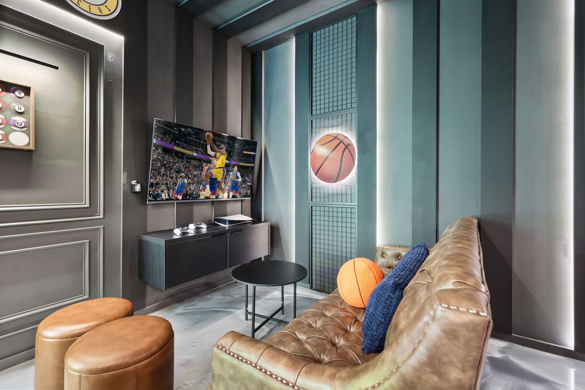 Una sala de estar moderna con un sofá de cuero, un televisor montado en la pared y decoración con temática de baloncesto.