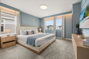 Ein Schlafzimmer mit Bett, Nachttischen, einem Fenster mit Vorhängen und einem an der Wand befestigten Fernseher.