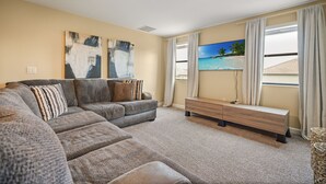 Una sala de estar con un sofá modular, un televisor de pantalla plana y obras de arte en la pared.