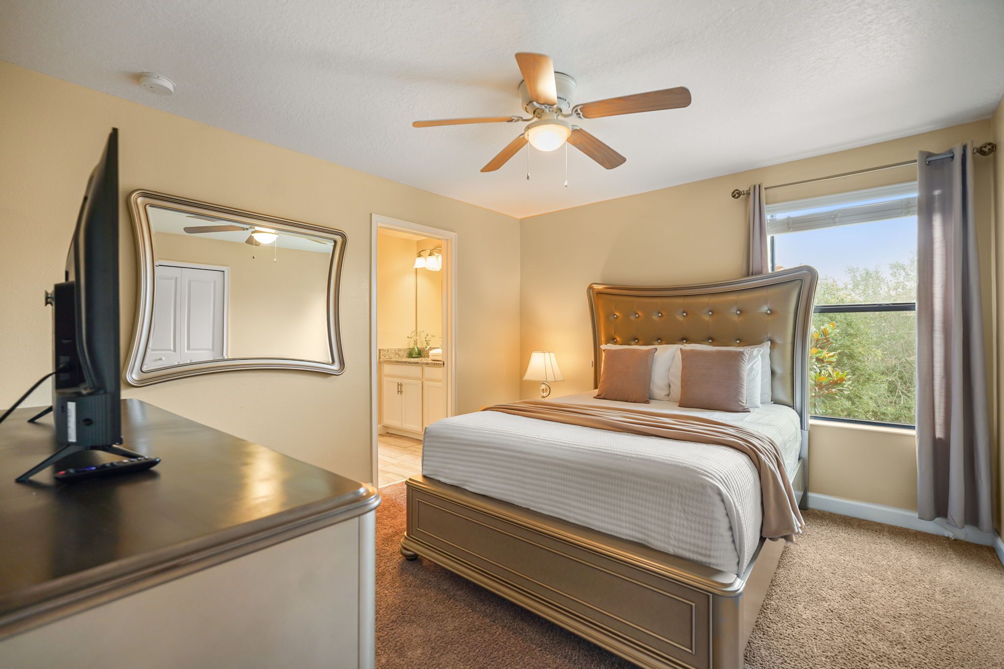 A bedroom with a bed, a ceiling fan, a dresser, and a window with curtains.