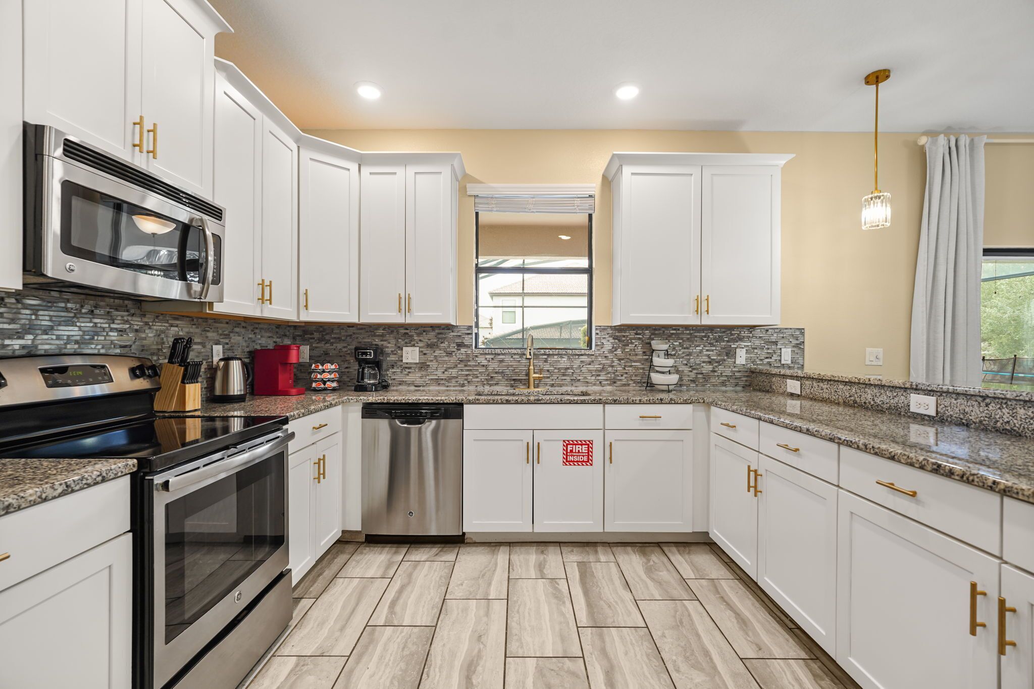 A modern kitchen with white cabinets, stainless steel appliances, a granite countertop, and a tiled backsplash.