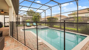 Una piscina techada al aire libre con una cerca de seguridad, sillas de descanso y una zona de patio.