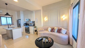 A modern living room with a sofa, a coffee table, and a kitchen area with a refrigerator, stove, and microwave. - Cana Life | Tropical Haven 2 (Punta Cana)