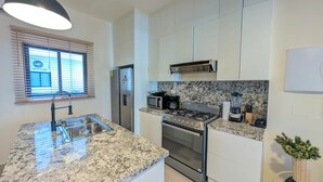 A modern kitchen with granite countertops, stainless steel appliances, and a window with blinds. - Cana Life | Tropical Haven 2 (Punta Cana)