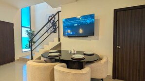 A modern dining area with a TV mounted on the wall, a staircase, and a view of the outdoors. - Cana Life | Tropical Haven 2 (Punta Cana)