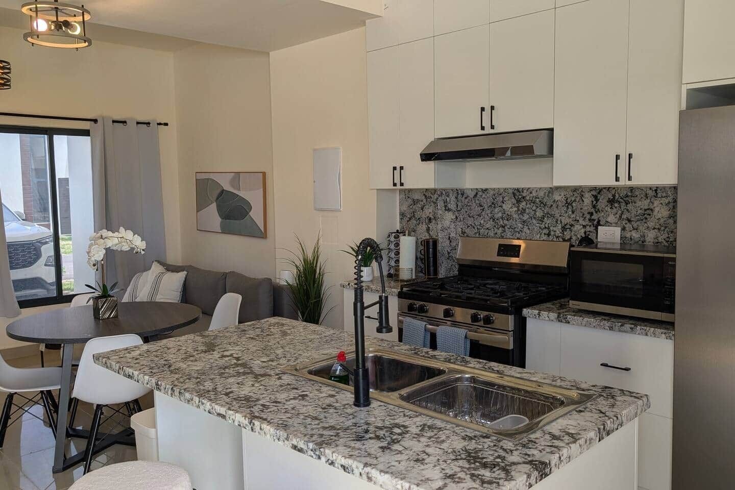 Een moderne keuken met granieten aanrechtbladen, roestvrijstalen apparatuur en een eethoek met een ronde tafel en stoelen.