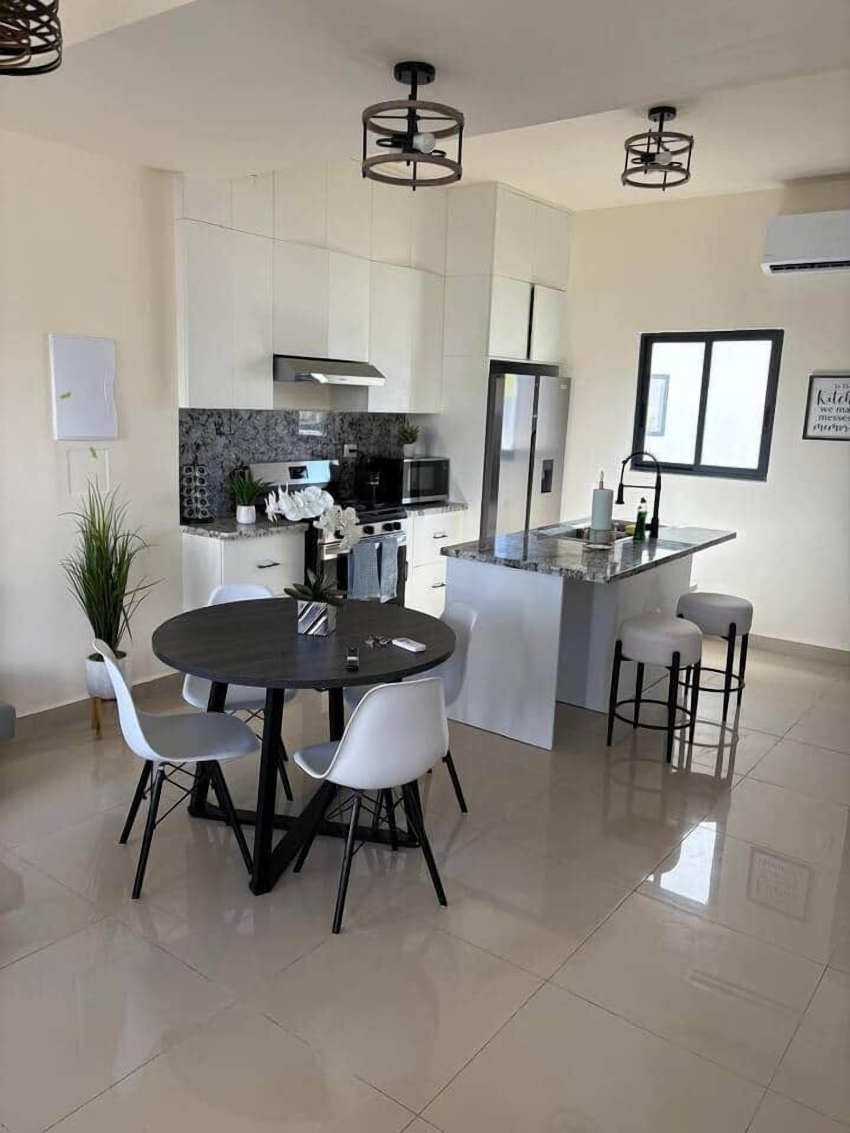 Une cuisine moderne avec des meubles blancs, un îlot central et un coin repas comprenant une table ronde et des chaises.