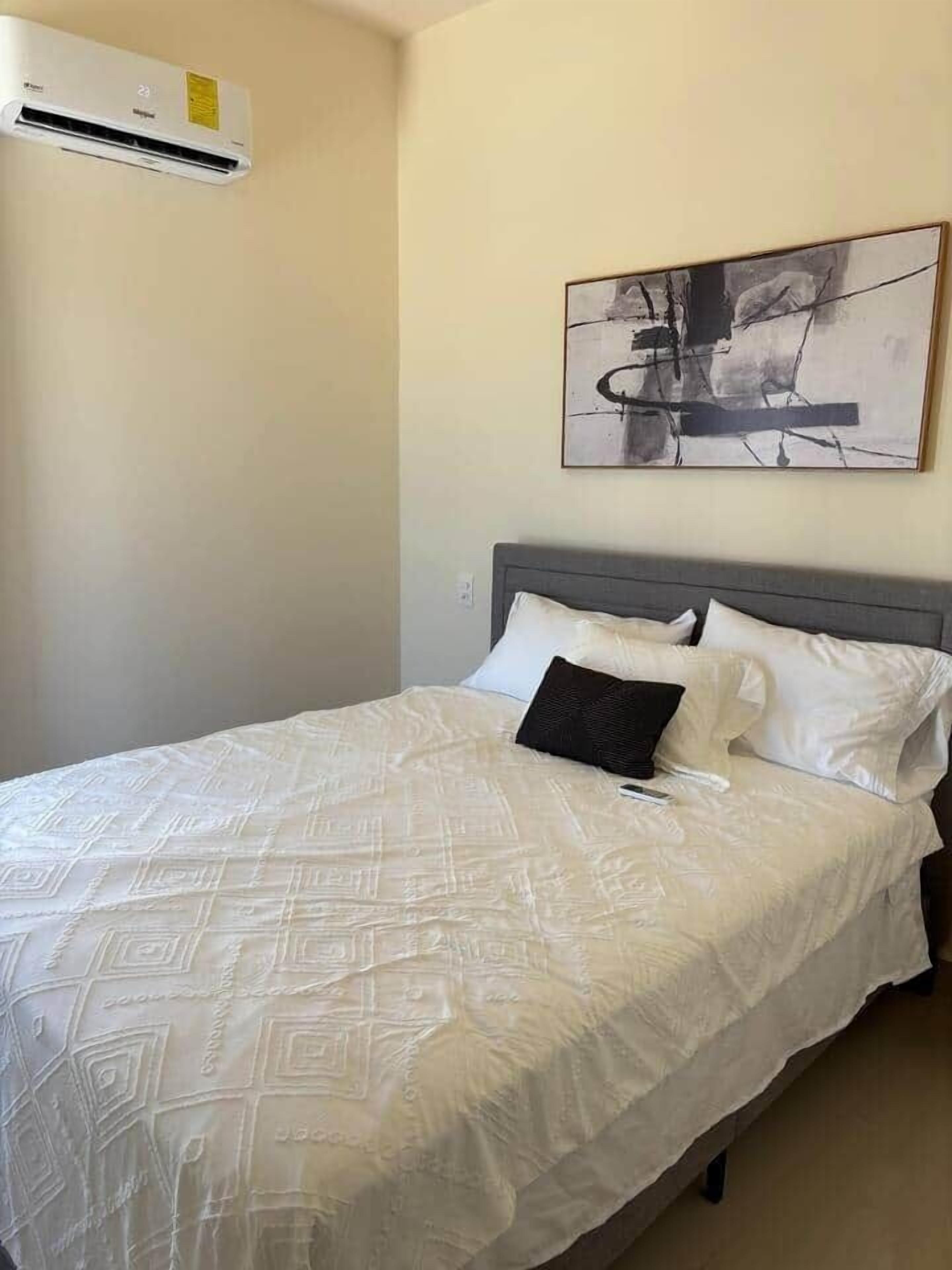 Ein Schlafzimmer mit einem Bett, einer Wand-Klimaanlage und einem abstrakten Kunstwerk.