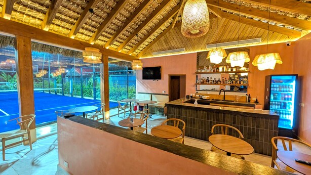 A bar area with wooden furniture, a TV, and a beverage dispenser. - Cana Life Breeze | Blue Coral Residences C1 (Punta Cana)