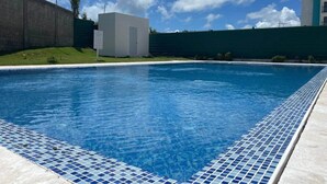 A swimming pool with a tiled edge, a concrete wall, and a building in the background. - Cana Life Breeze | Blue Coral Residences C1 (Punta Cana)