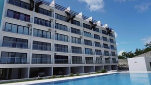 A multi-story hotel with a swimming pool in front. - Cana Life Breeze | Blue Coral Residences C1 (Punta Cana)