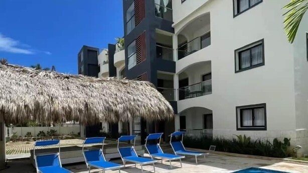 Una piscina con agua azul, rodeada de sillas de descanso y una estructura de techo de paja.