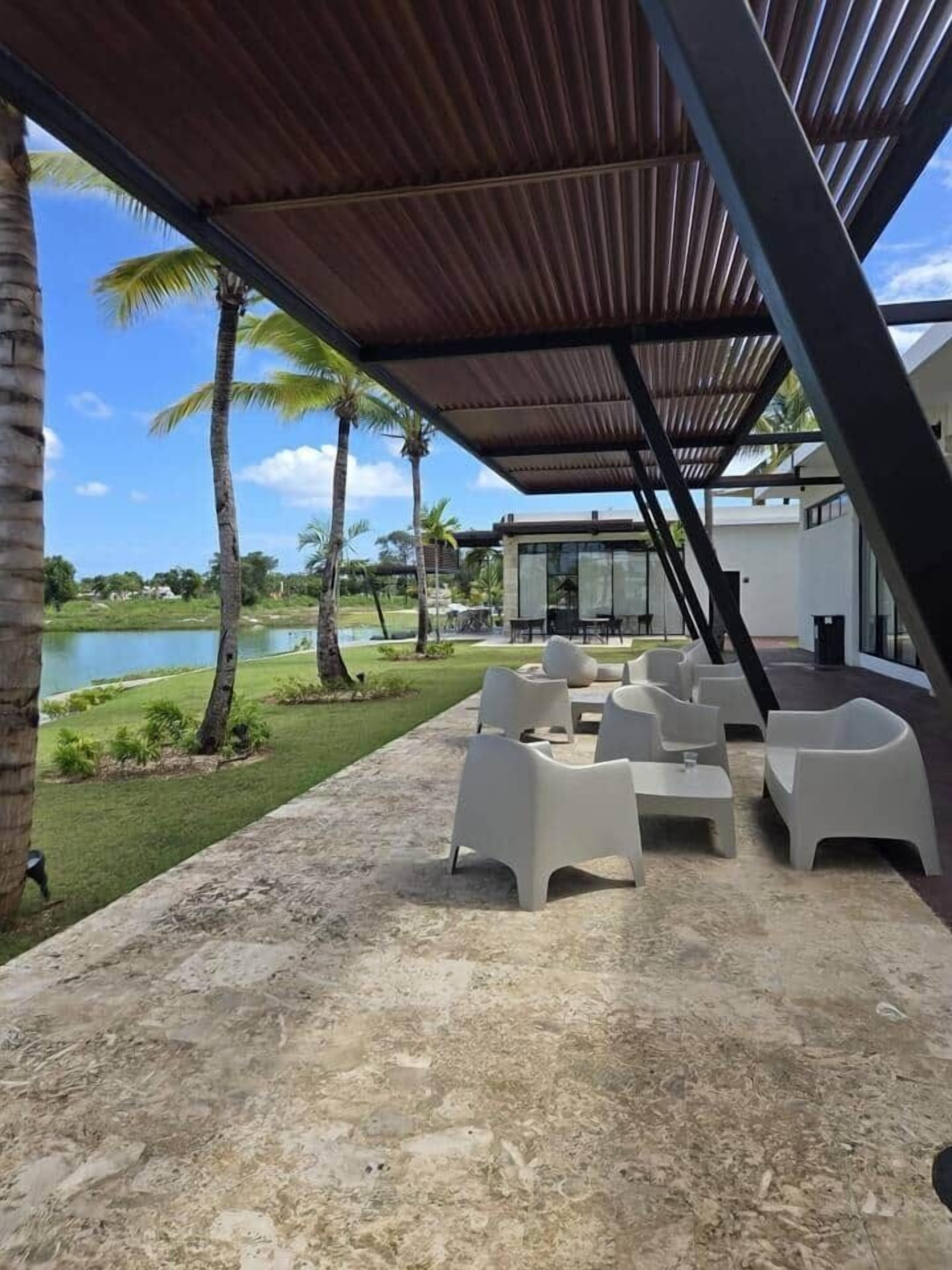 A covered outdoor seating area with modern white chairs, a pool, and palm trees in the background.