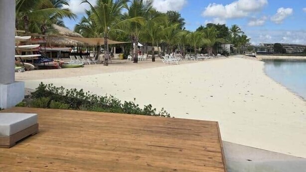 Une plage avec une terrasse en bois, des palmiers et un ciel dégagé.