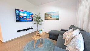 Ein modernes Wohnzimmer mit Flachbildfernseher, grauem Sofa, blauem Teppich und einem Gemälde mit Strandmotiv.
