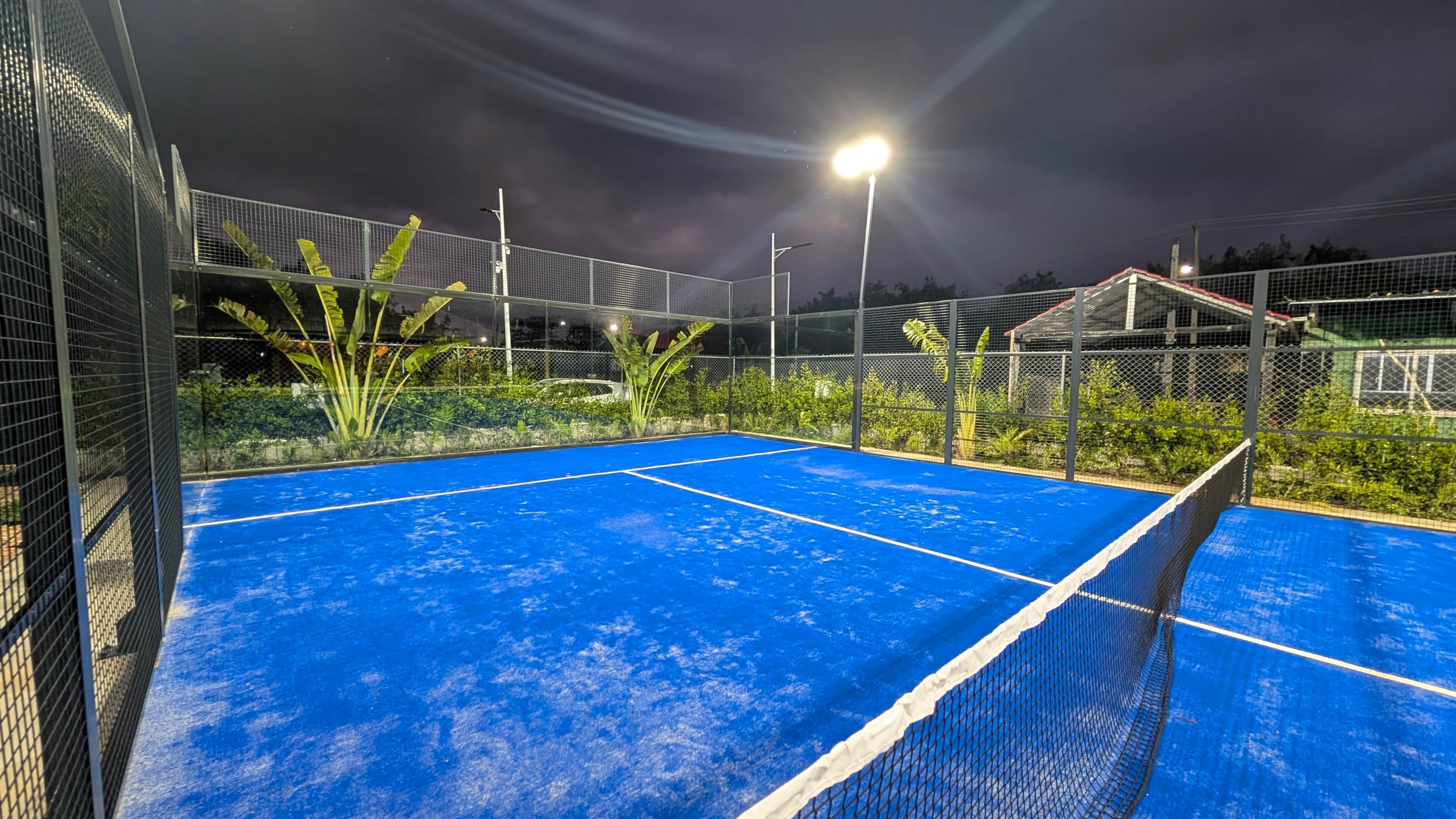 Un campo da tennis con rete, circondato da una recinzione e illuminato da luci sopraelevate.