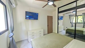 Ein Schlafzimmer mit einem Bett, einem Schminktisch, einem an der Wand befestigten Fernseher und einem Deckenventilator.