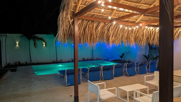Un área de piscina con techo de paja, luces colgantes y sillones de descanso.