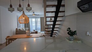 A modern kitchen with a white countertop, hanging pendant lights, a wooden ladder, and a potted plant. - Cana Life Luxury | Azure Sky Penthouse (Punta Cana)