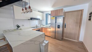 A modern kitchen with a marble countertop, stainless steel appliances, and wooden cabinets. - Cana Life Luxury | Azure Sky Penthouse (Punta Cana)