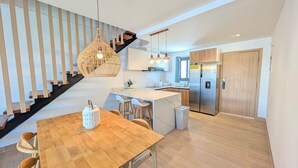 A modern kitchen with a wooden island, stainless steel appliances, and a staircase with wooden railings. - Cana Life Luxury | Azure Sky Penthouse (Punta Cana)