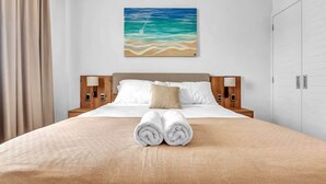 Ett hotellrum med en säng, en tavla som föreställer en strandscen och en prydligt vikt handduk på sängen.