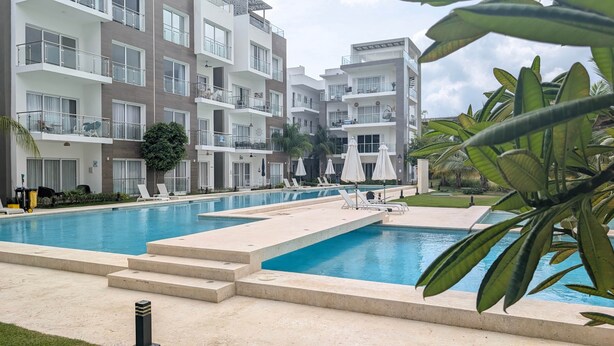 Un hotel moderno con piscina, numerosi balconi e vegetazione rigogliosa.