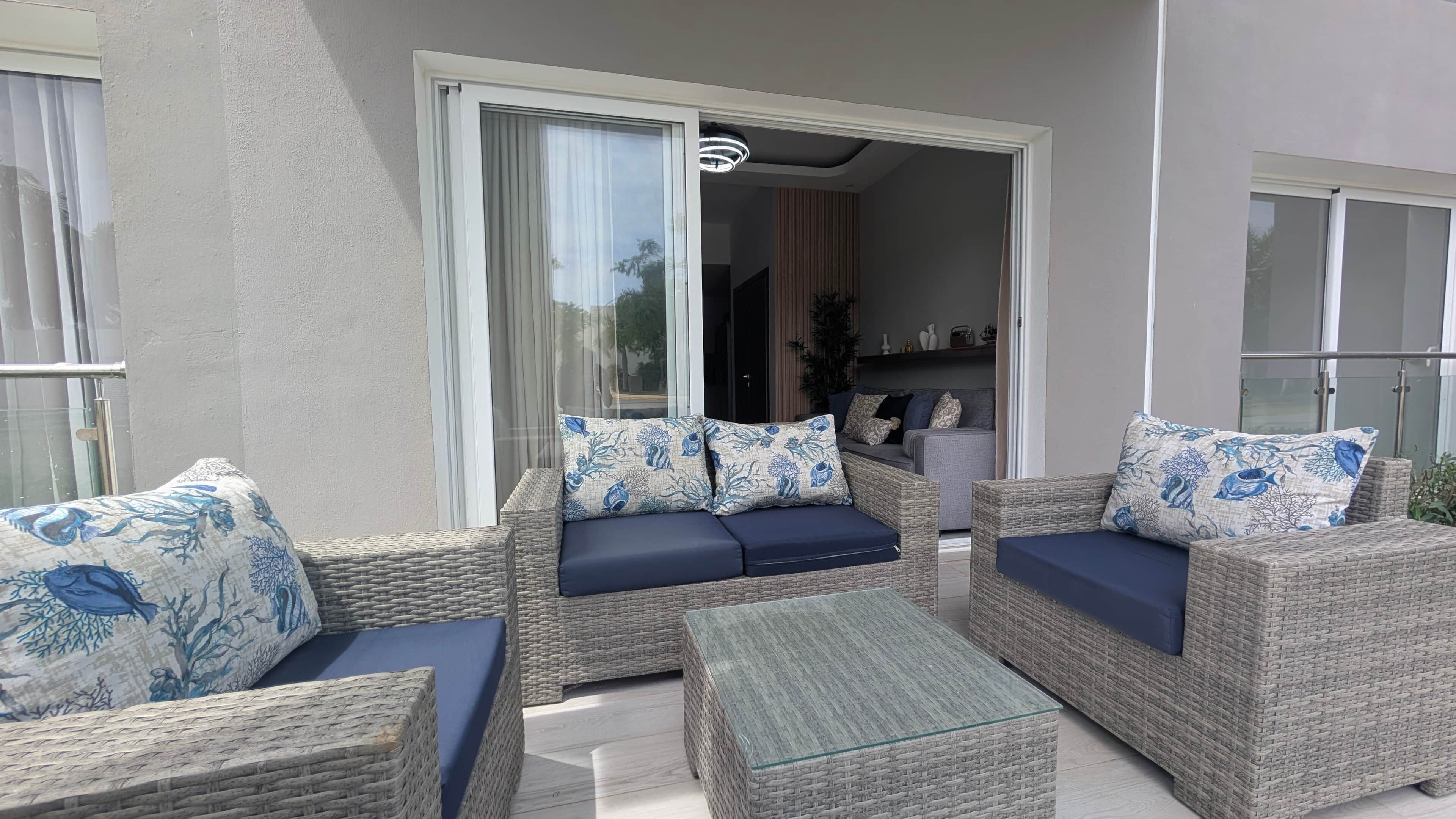 A balcony with wicker furniture, a glass coffee table, and a sliding glass door leading to an interior space.