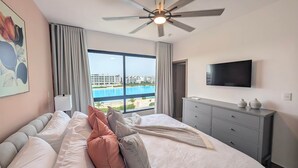 Habitación de hotel con cama, televisión, cómoda y vistas a una piscina y edificios.