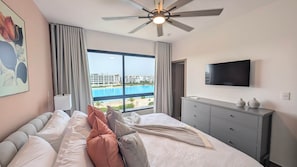 Ein Hotelzimmer mit Bett, Fernseher, Kommode und Blick auf einen Pool sowie Gebäude.