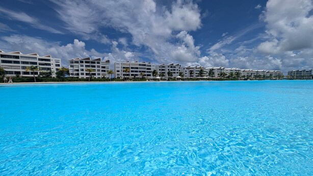 Un resort con una piscina azul cristalina, edificios blancos y una playa.