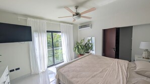 Een slaapkamer met een bed, een plafondventilator, een kamerplant, een televisie en een deur.