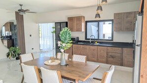 Een moderne keuken met houten kastjes, een eettafel met stoelen en hanglampen.