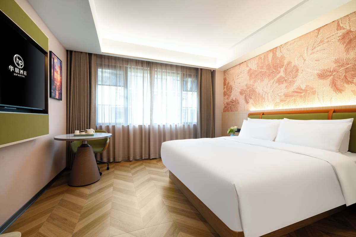 A hotel room with a bed, a TV, a small table, and a window with curtains.
