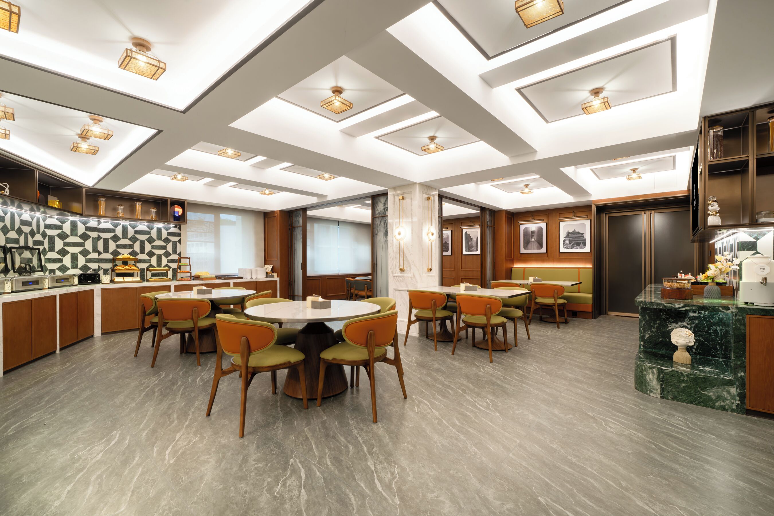Un moderno vestíbulo de hotel con una mesa redonda central, varias zonas de estar y una cocina.