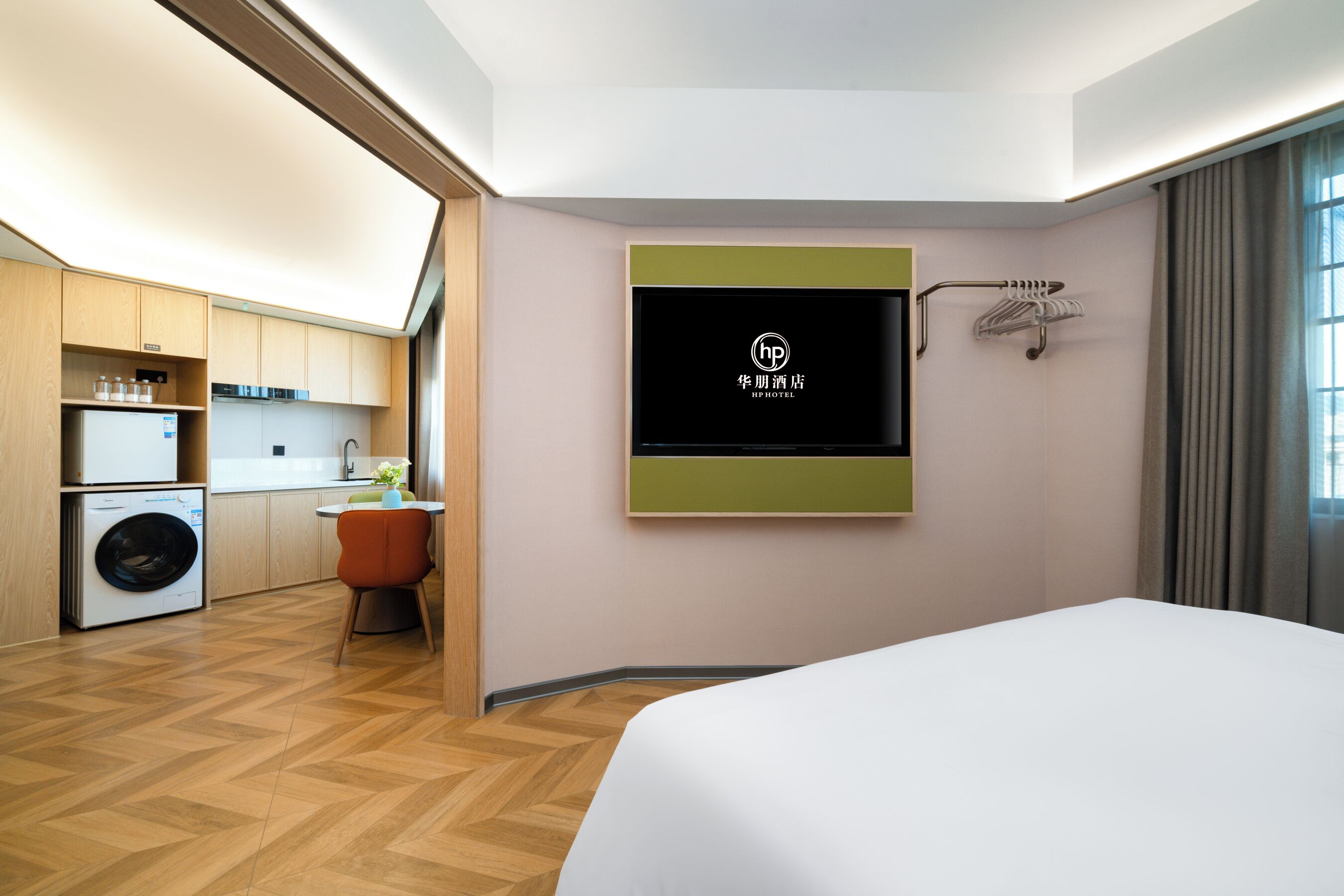 Ein Hotelzimmer mit Bett, Wandfernseher, Waschmaschine und einer kleinen Küchenzeile.